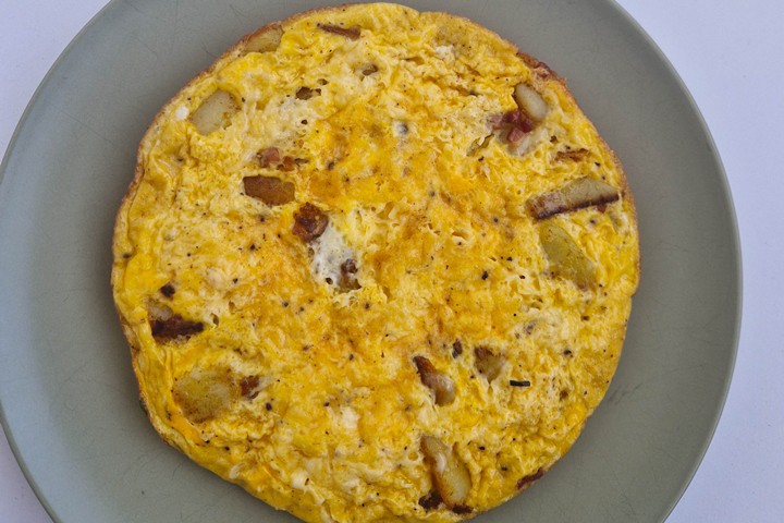 Golden-brown potato and bacon omelette served on a light green plate, showcasing a delicious and hearty meal.