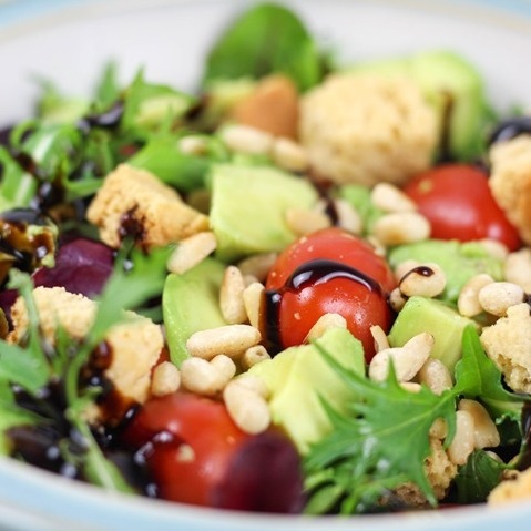 Fresh salad with cherry tomatoes, avocado, pine nuts, croutons, and greens drizzled with balsamic glaze.