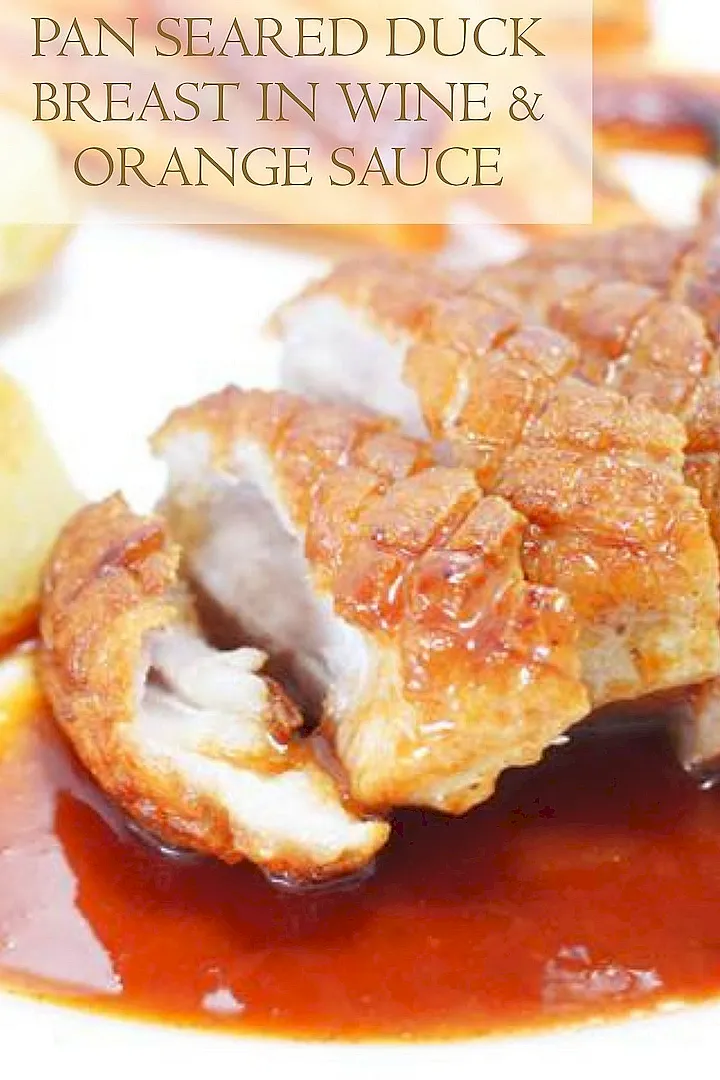 Pan seared duck breast in rich wine and orange sauce, showcasing crispy skin and succulent meat.