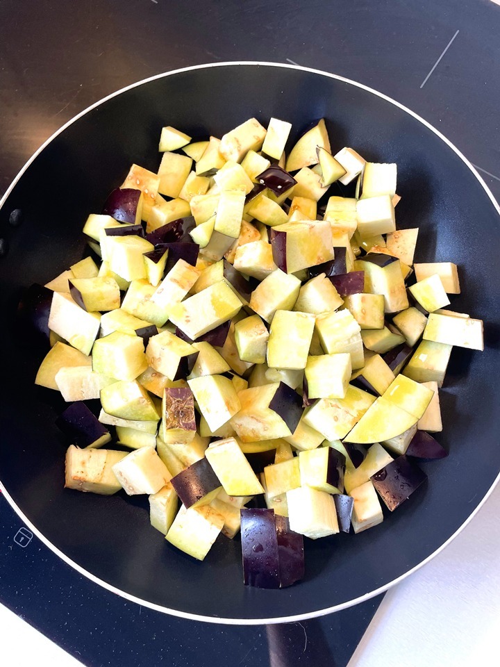 Chopped eggplant cubes in a black frying pan ready for cooking. Perfect for healthy vegetable recipes.