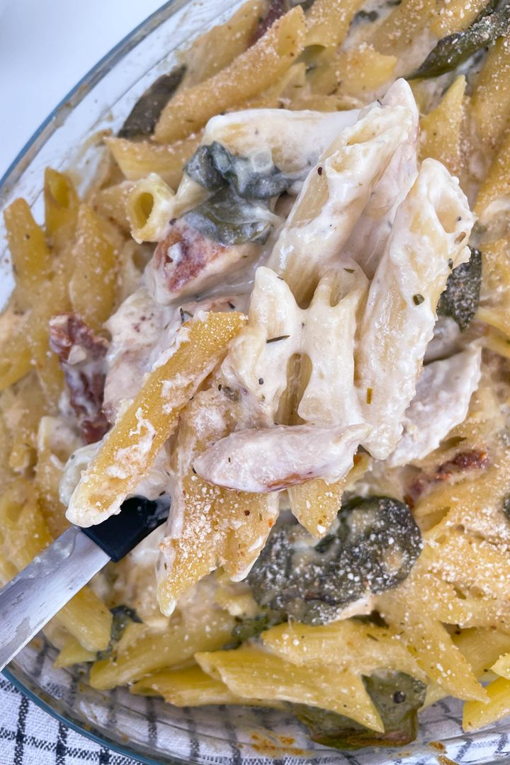 Creamy baked penne pasta with spinach and tomatoes, garnished with cheese in a glass dish.