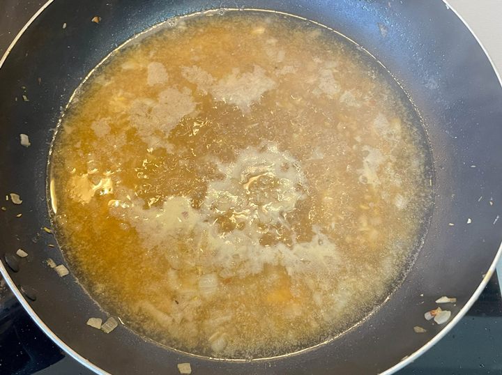 Simmering broth with onions in a black pan, perfect for a savory soup base or flavorful sauce.