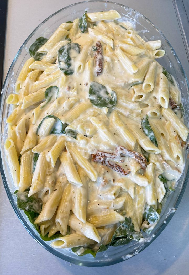 Creamy penne pasta with spinach and sun-dried tomatoes in a cheesy sauce, served in a glass dish.