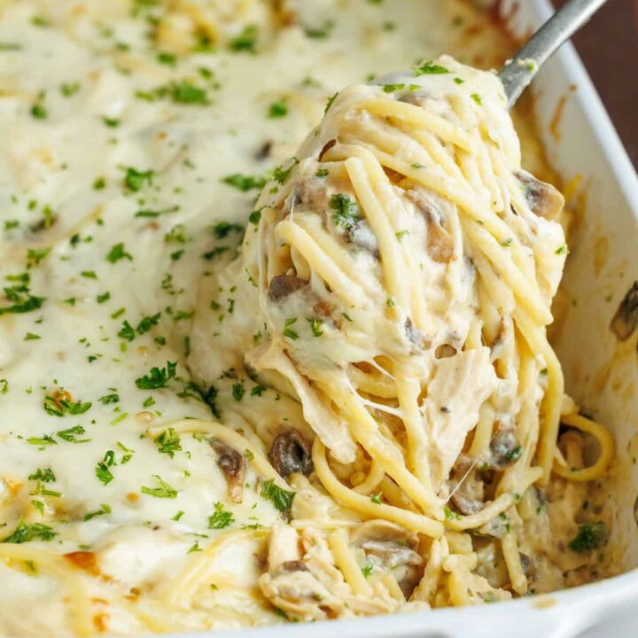 Creamy baked spaghetti with mushrooms and cheese in a white dish, garnished with fresh parsley.