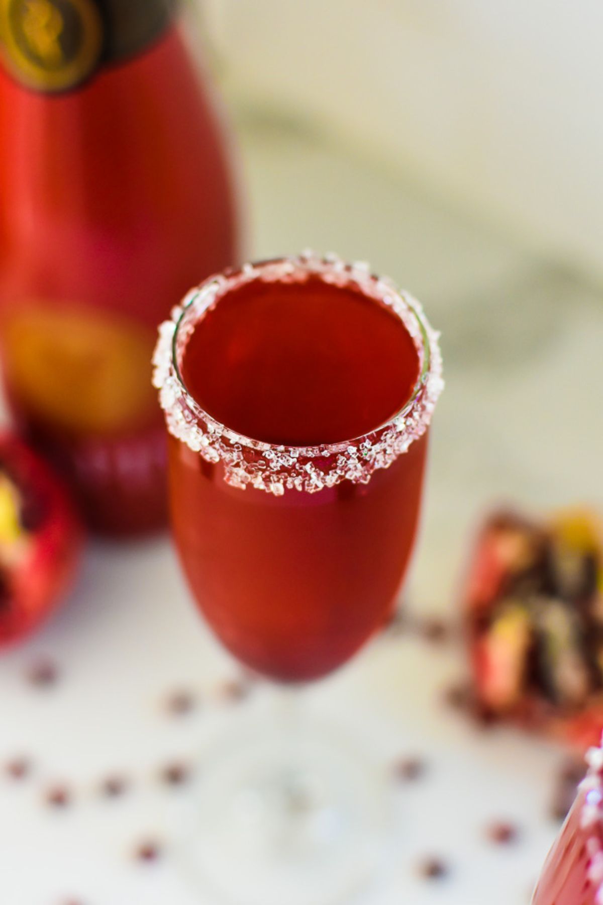 Sparkling red cocktail in flute with sugar rim, beside a pomegranate. Perfect festive drink.