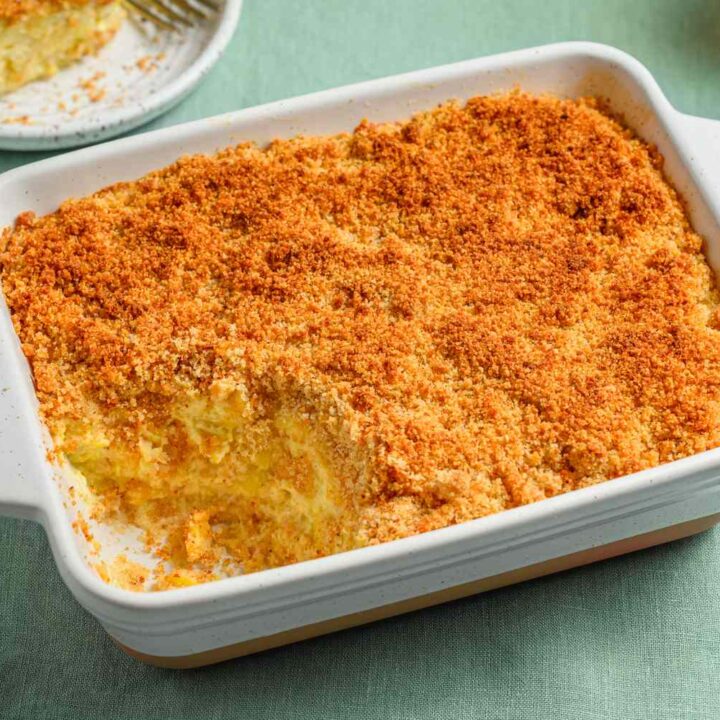 Golden-brown baked casserole with breadcrumb topping in white dish on green tablecloth.
