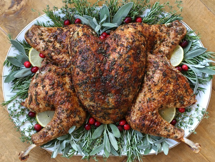 Herb-roasted spatchcocked turkey with lemon, fresh herbs, and cranberries on a platter, ideal for festive dinners.