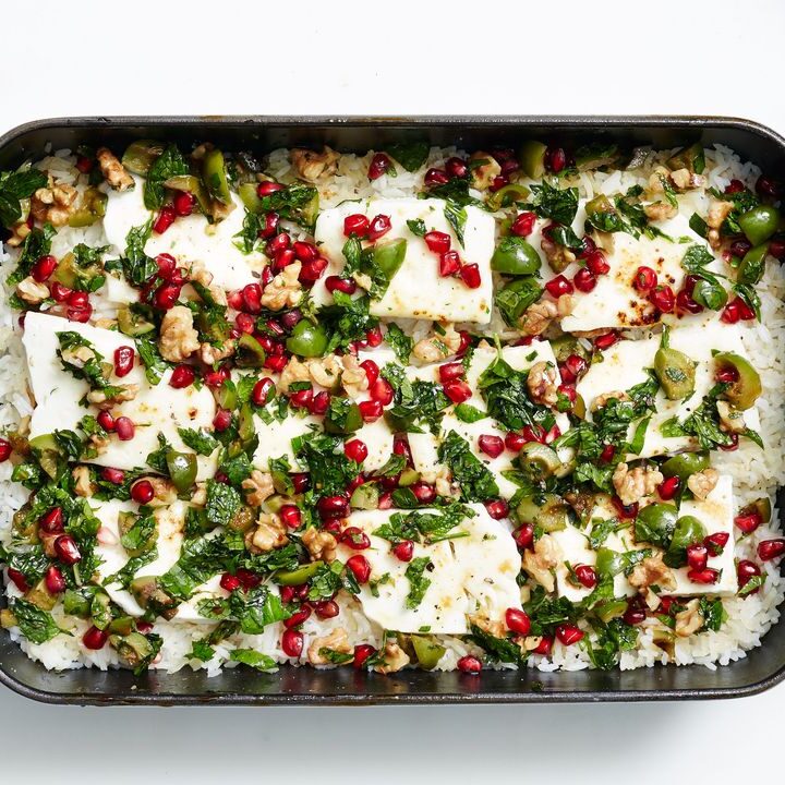 Baked halloumi with rice, walnuts, pomegranate seeds, and herbs in a Staub dish on a white background.