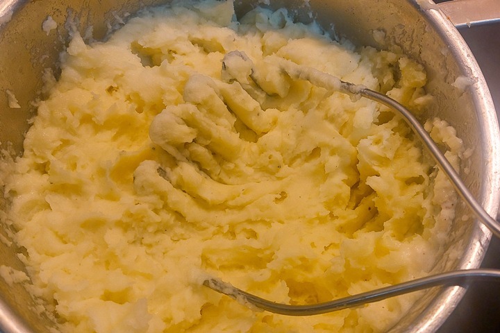 Creamy mashed potatoes in a pot with a masher, ready to serve.