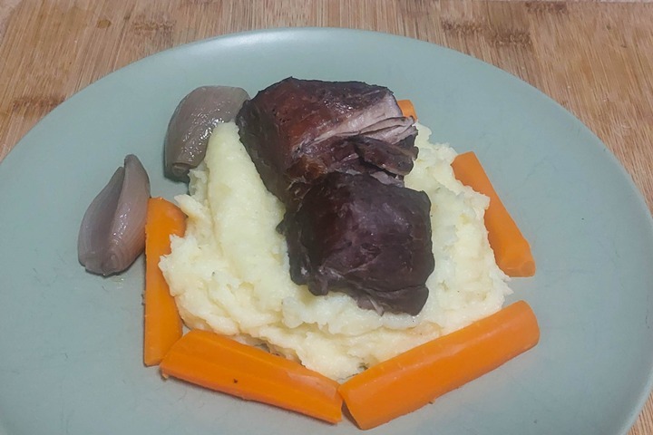 Slow-cooked beef on creamy mashed potatoes with carrots and onions, served on a plate for a hearty meal.