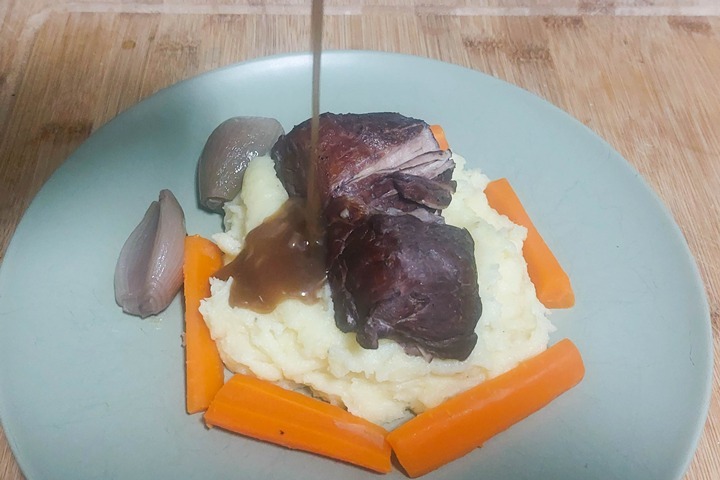 Tender pork served with rich gravy on mashed potatoes, garnished with carrots and onions on a plate.