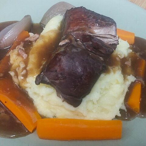 Savoury braised pork with mashed potatoes, carrots, and rich gravy on a plate. Comfort food dinner dish.