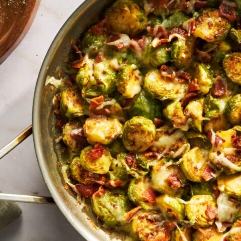 Cheesy Brussels sprouts with crispy bacon in skillet, served fresh and delicious. Perfect savory side dish.