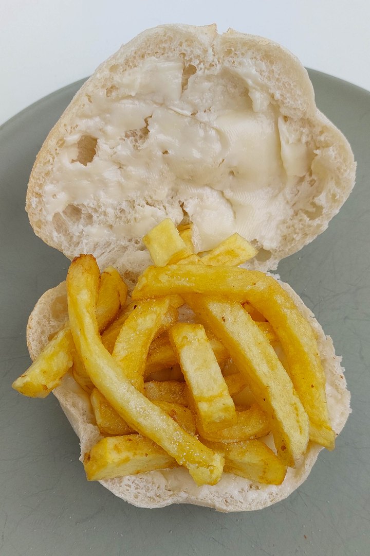 Bread roll with butter filled with crispy golden fries on a plate.