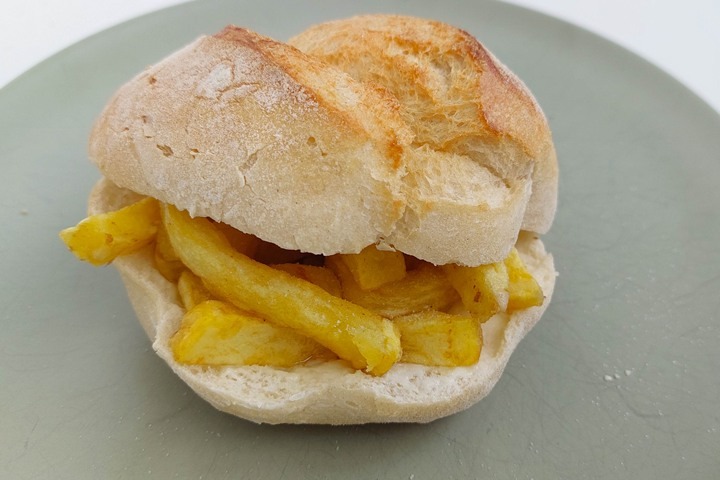 Crispy chip butty on a fresh bread roll, placed on a grey plate, ideal for a delicious snack or lunch.