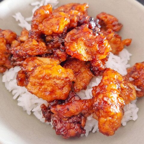 Crispy chicken coated in sweet sauce served over a bed of fluffy white rice in a bowl. Perfect for a delicious meal.