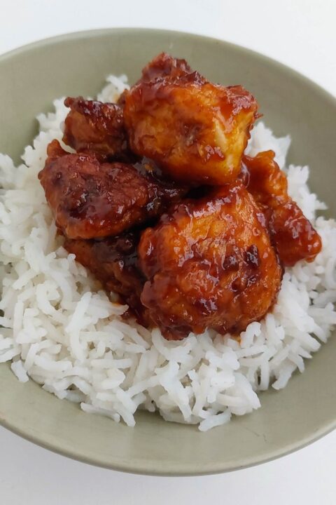 Spicy glazed chicken on fluffy white rice in a bowl, perfect tasty Asian dish for lunch or dinner.