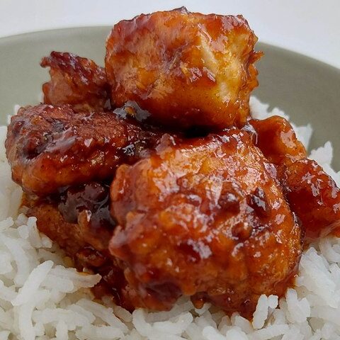 Spicy glazed chicken on a bed of fluffy white rice in a bowl, showcasing a delicious savory dish ready to enjoy.