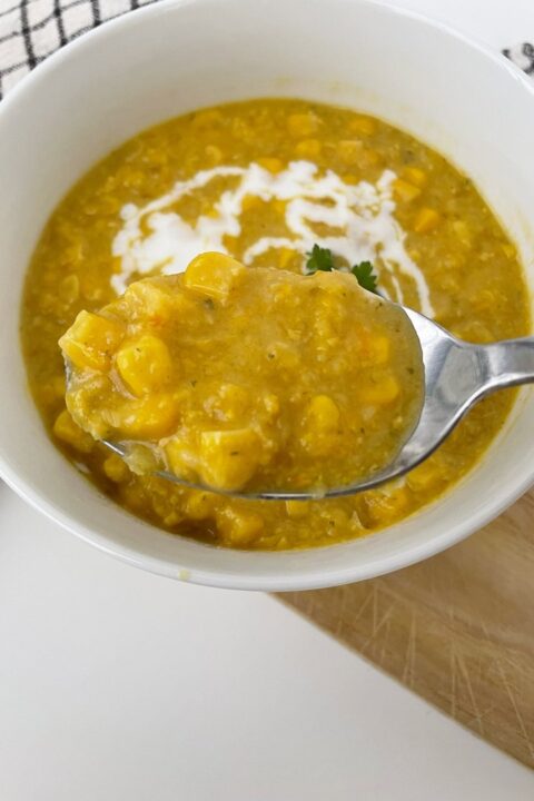 Creamy corn soup in a white bowl with a spoonful of soup, garnished with herbs. Perfect for a cozy meal.