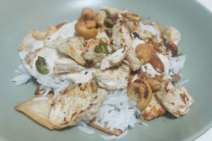 Grilled chicken with nuts over basmati rice and pita on a green plate.