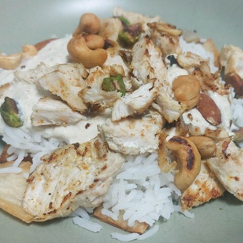 Grilled chicken with nuts and rice on a plate, garnished with cashews and pistachios.