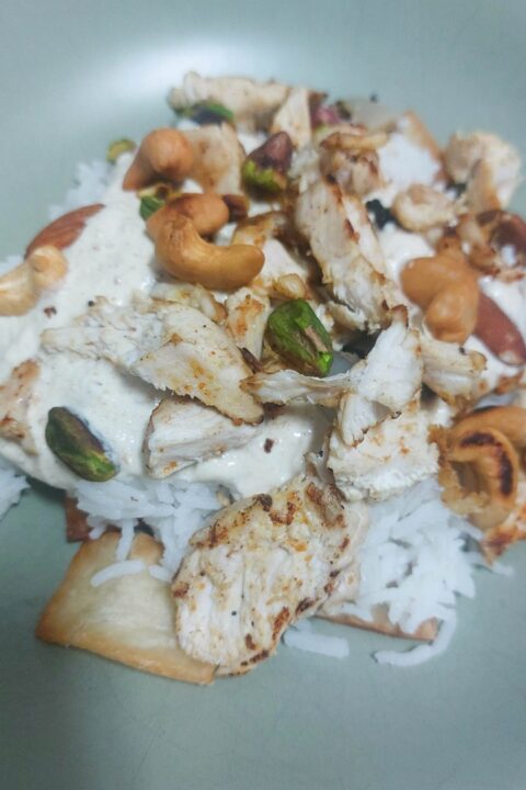 Grilled chicken with creamy sauce over basmati rice, garnished with cashews and pistachios.