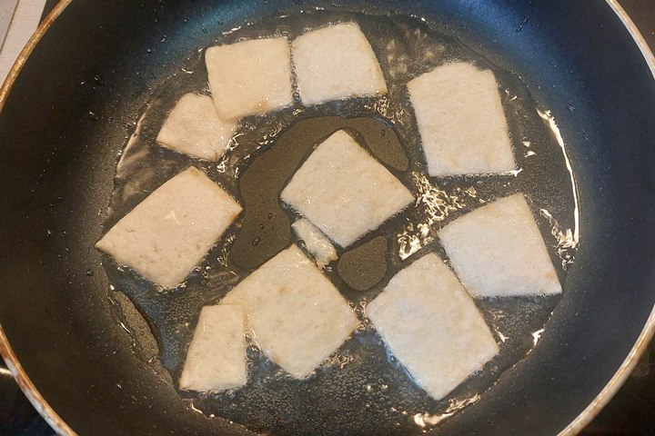 Slices of pita frying in a pan with oil, showcasing a delicious cooking process.