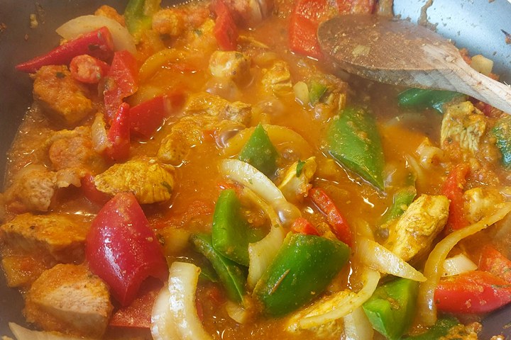 Colorful chicken stew simmering with bell peppers and onions in a pot, garnished with spices for a delicious meal.