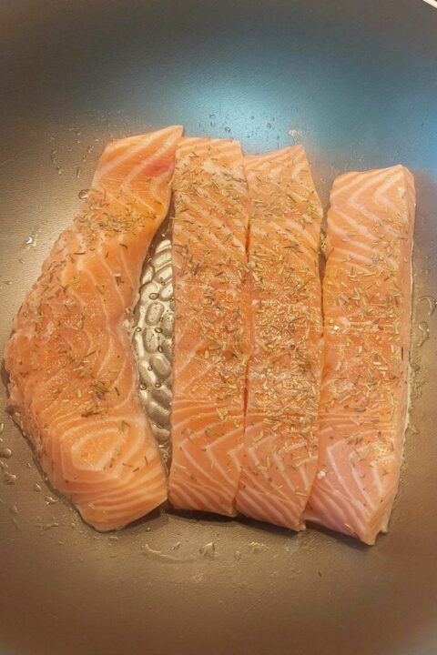 Raw salmon fillets seasoned with herbs in a pan, ready for cooking.