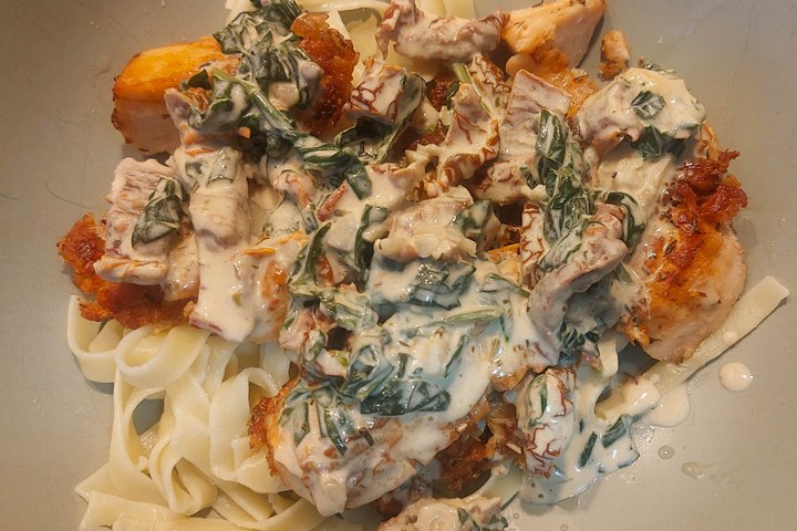 Delicious creamy chicken pasta with spinach and sauce, served on a gray plate. Perfect comfort food dish.