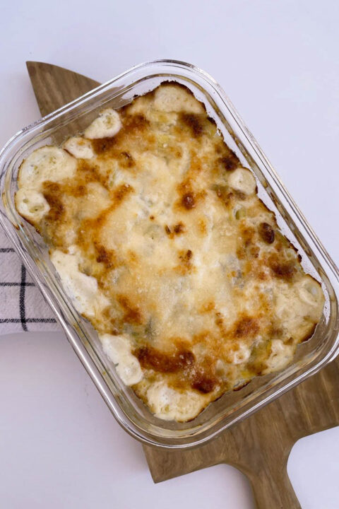Creamy baked artichoke dip with a golden crust, served on a wooden cutting board. Perfect comfort food!