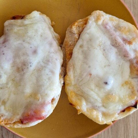 Two baked mini pizzas with melted cheese and ham on a yellow plate, resting on a wooden table.