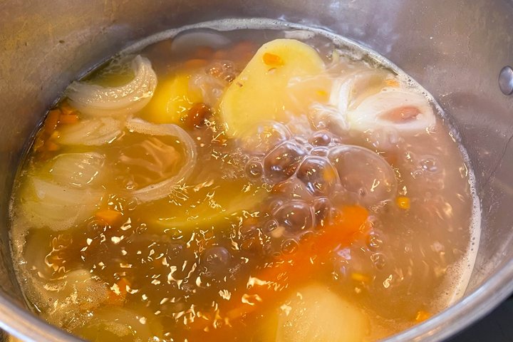 Warm vegetable soup simmering in a pot, featuring onions, carrots, and potatoes bubbling in rich broth.