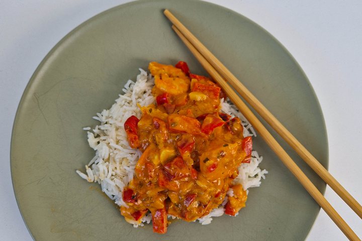 Delicious rice dish topped with colorful curry and peppers, served with chopsticks on a stylish plate.