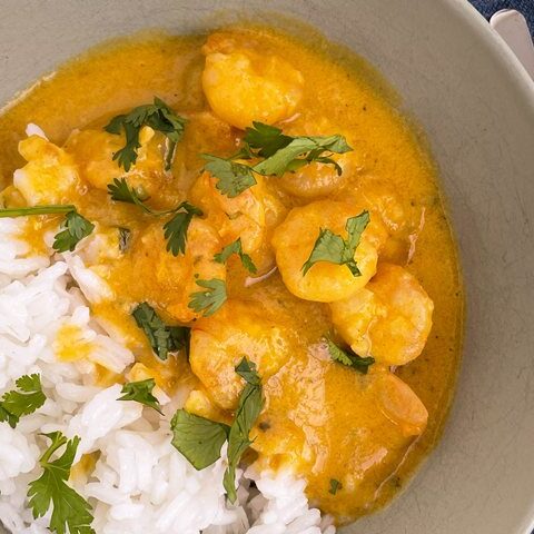 Delicious shrimp curry served with fluffy white rice, topped with fresh cilantro in a green bowl.