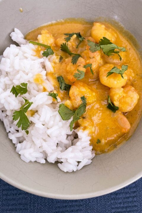 Delicious shrimp curry served with fluffy white rice, garnished with fresh cilantro in a light bowl.