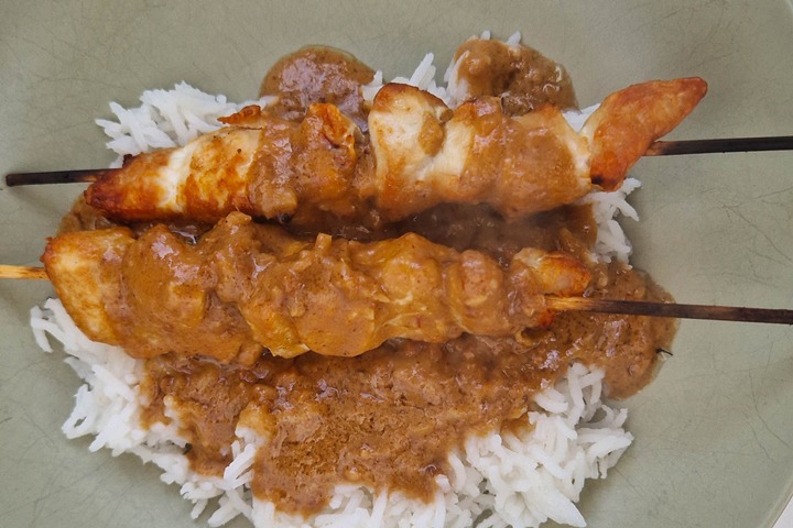 Delicious chicken skewers topped with rich peanut sauce served over fluffy rice on a green plate.