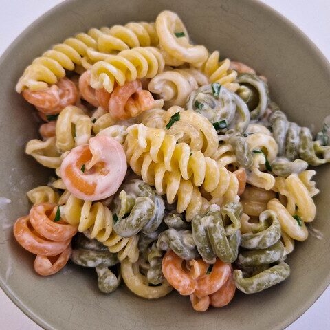 Colorful pasta salad with shrimp in a creamy dressing, served in a green bowl on a light background.