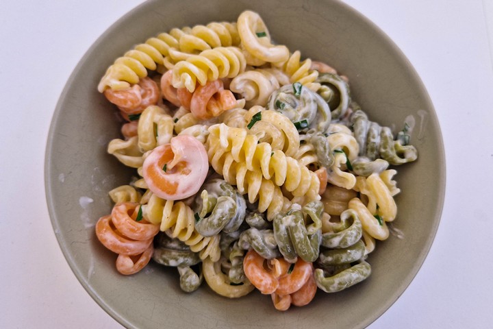 Colorful pasta salad with shrimp in a creamy dressing, served in a green bowl on a light background.
