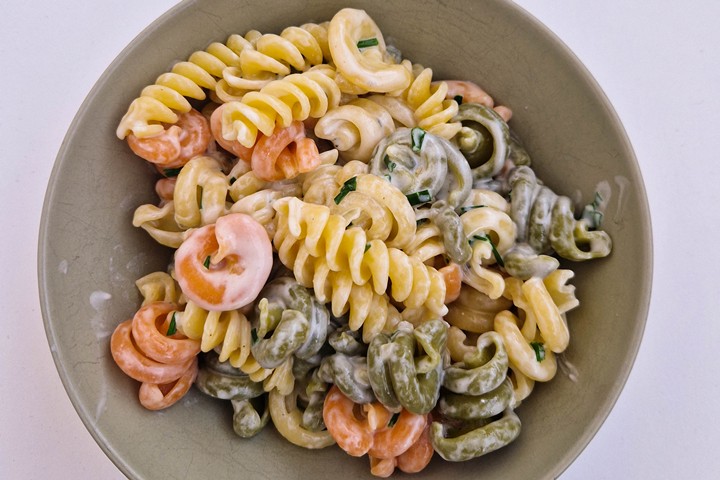 Colorful pasta with shrimp in a creamy sauce served in a bowl, garnished with herbs. Perfect for a delicious meal.