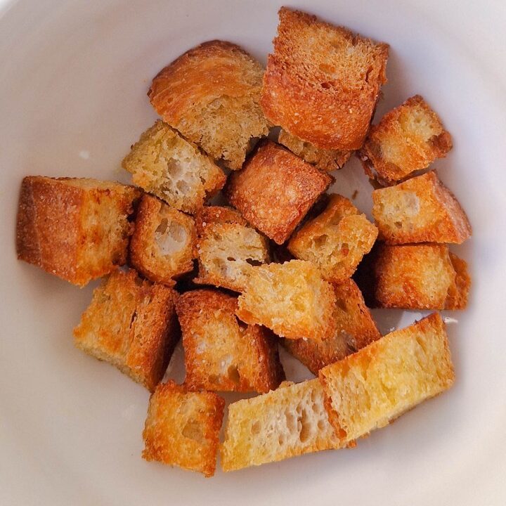 Toasted bread cubes in a white bowl, perfect for salads or soups, golden brown and crispy. Ideal for snacking.